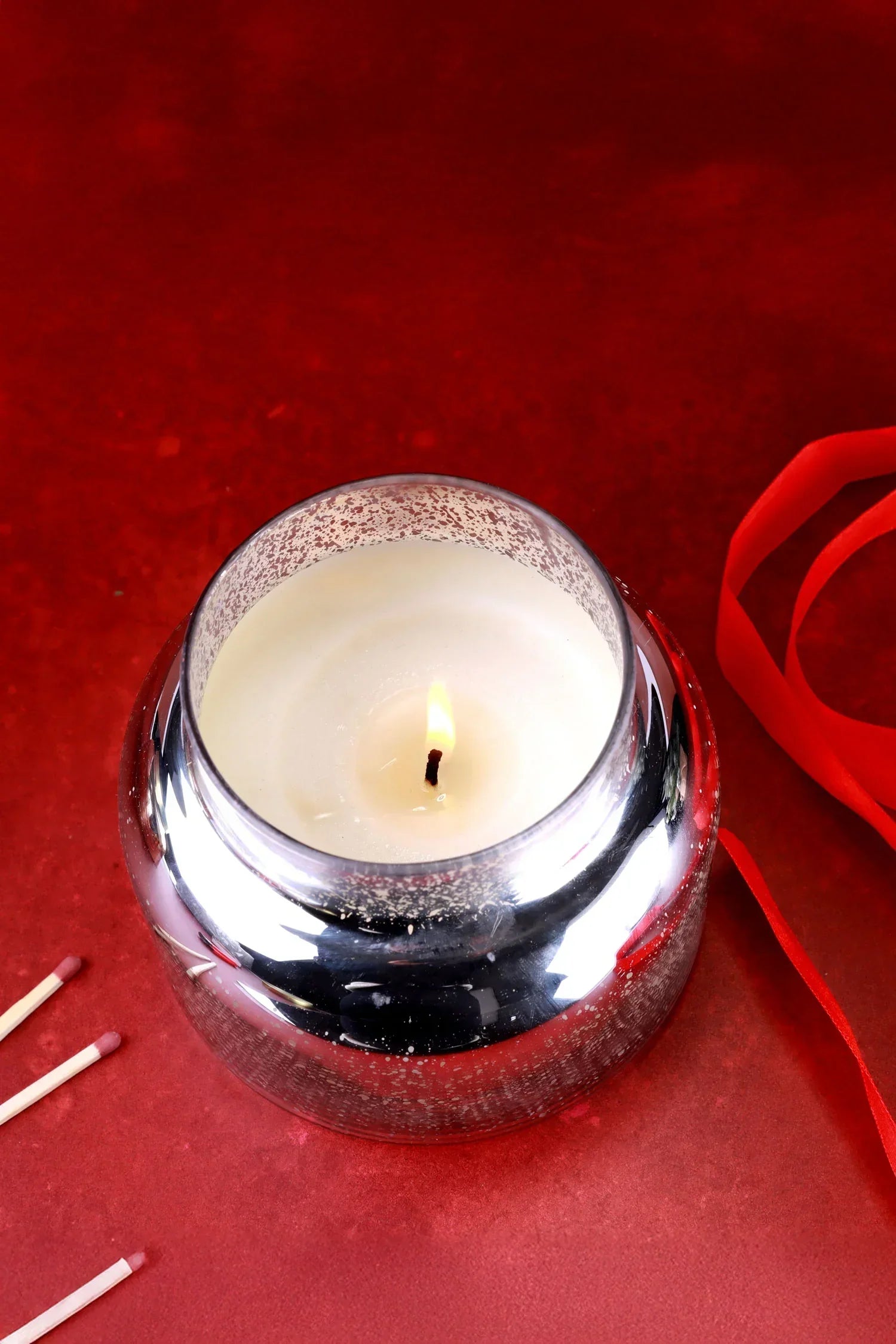 Luxury silver glass candle from G Decor burning on red table with ribbon and matches
