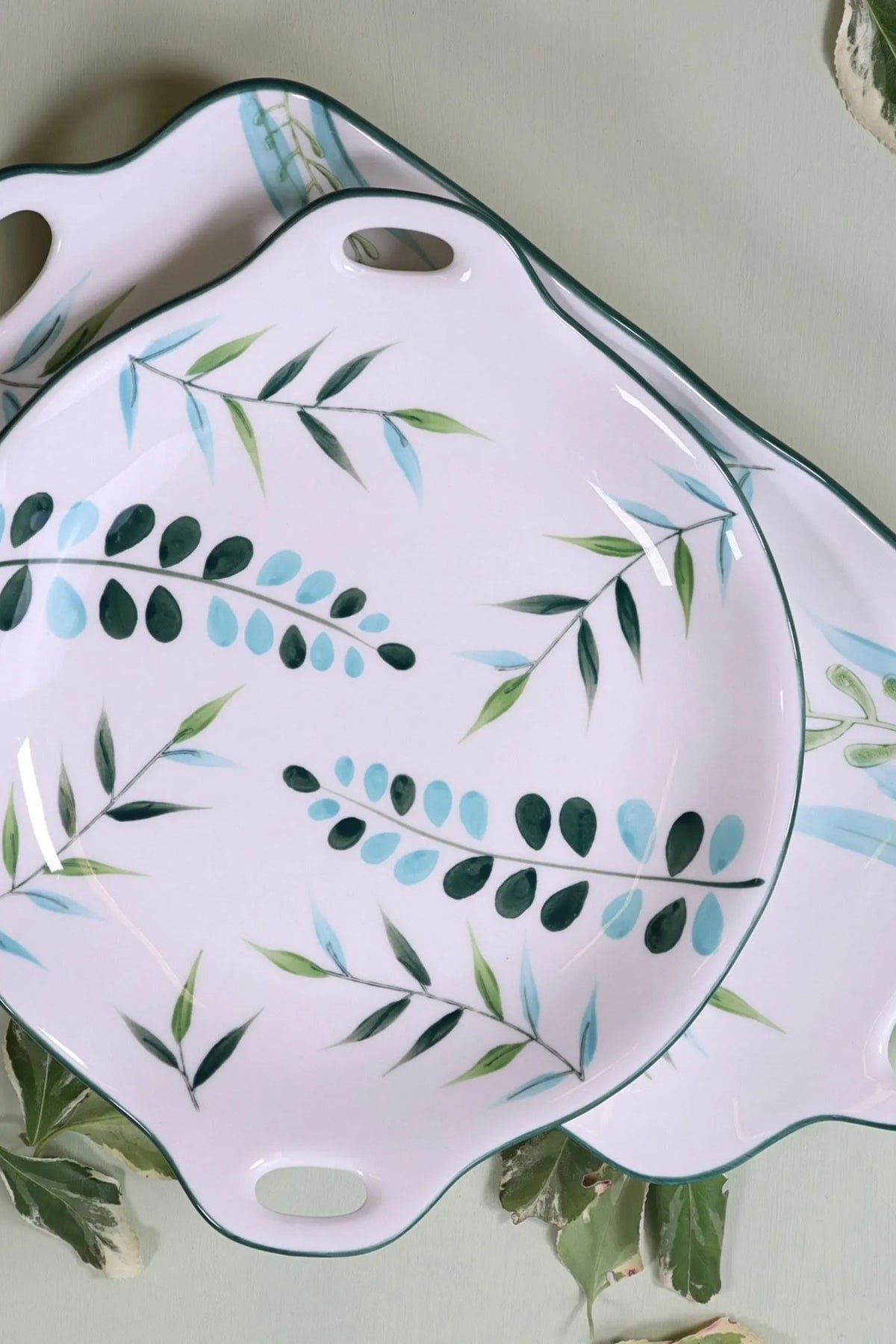 The round leaf plate resting on the long leaf platter, both white ceramic with green rims