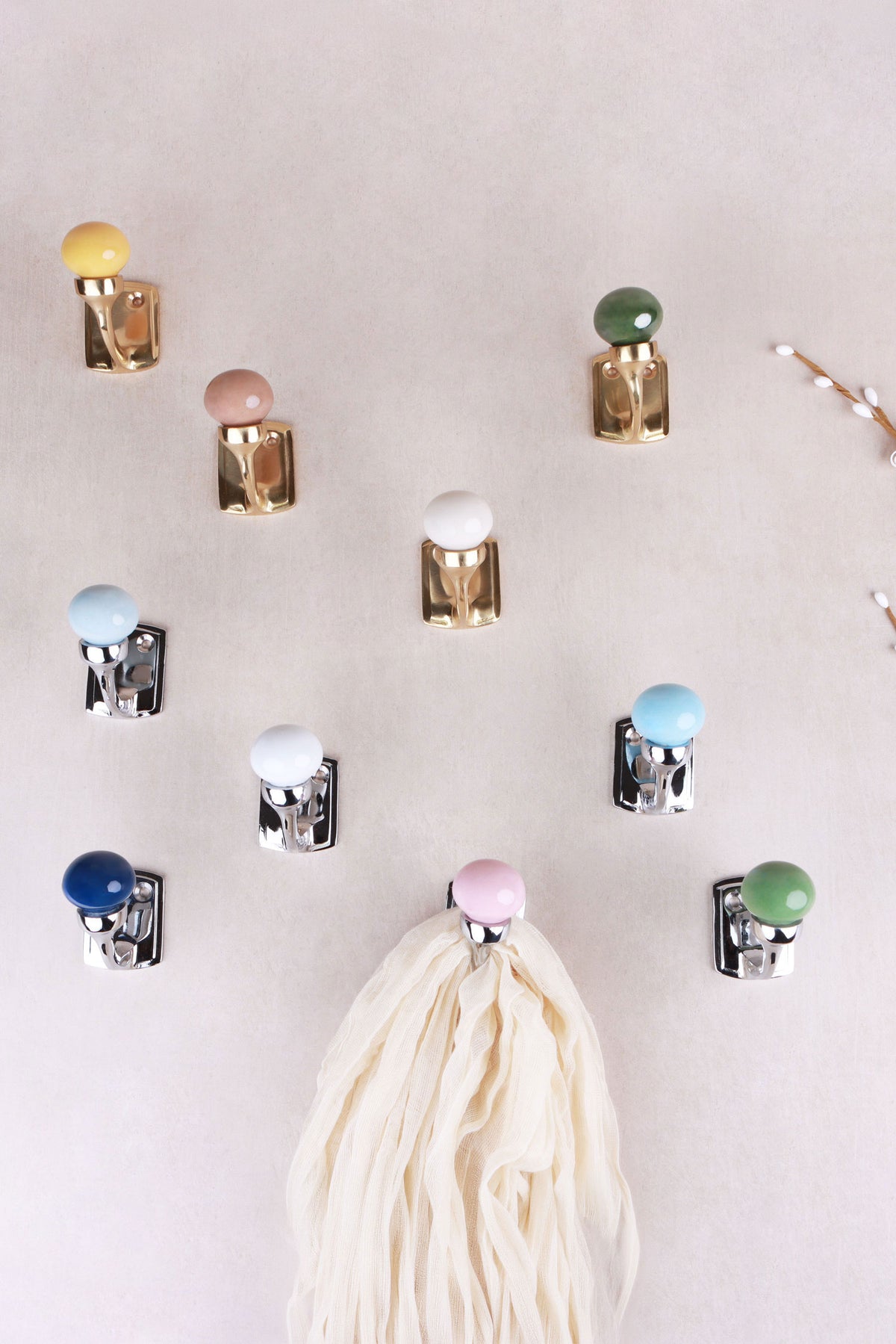Brass and chrome finish ceramic ball hooks spread across a pale wall, a cream scarf hanging from the light pink hook