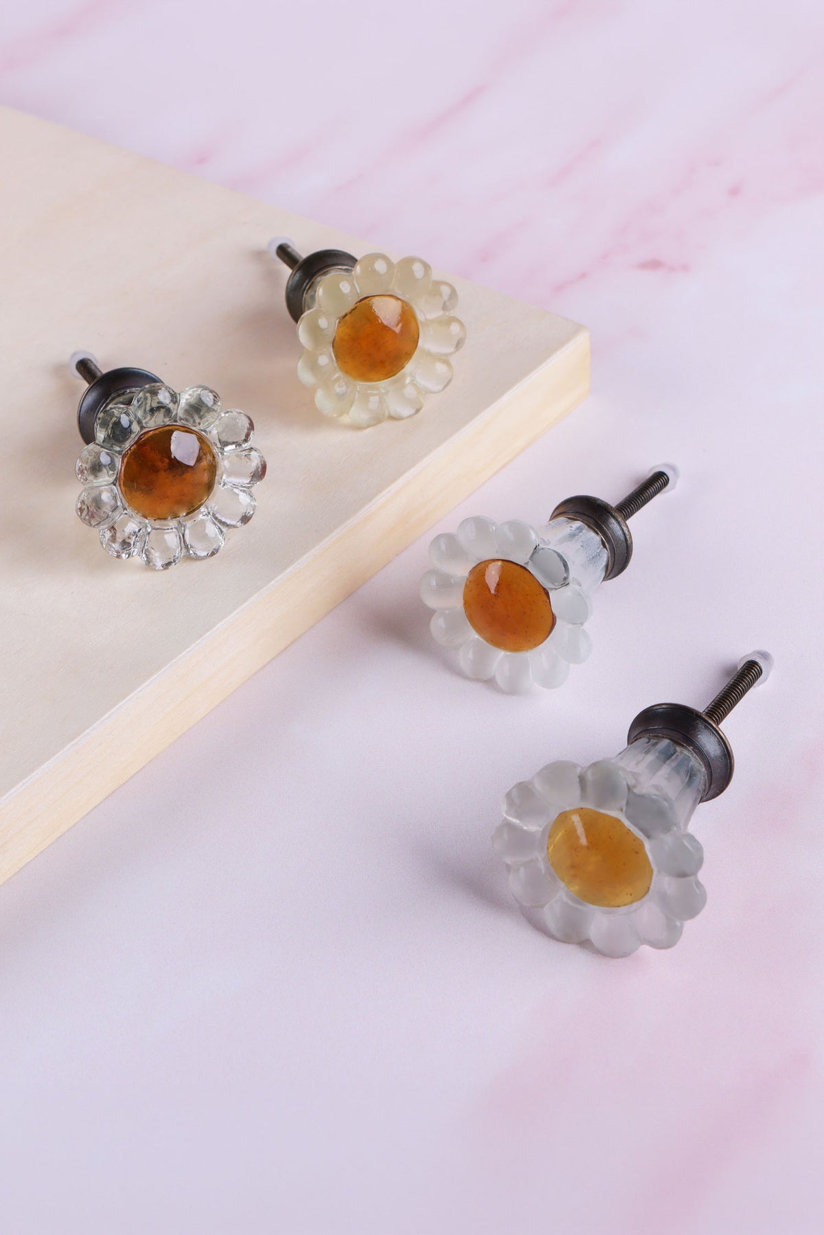 Daisy glass cabinet knobs with amber centres on antique brass finish bases: clear and ivory petals on a wooden board, frosted white and frosted grey petals below