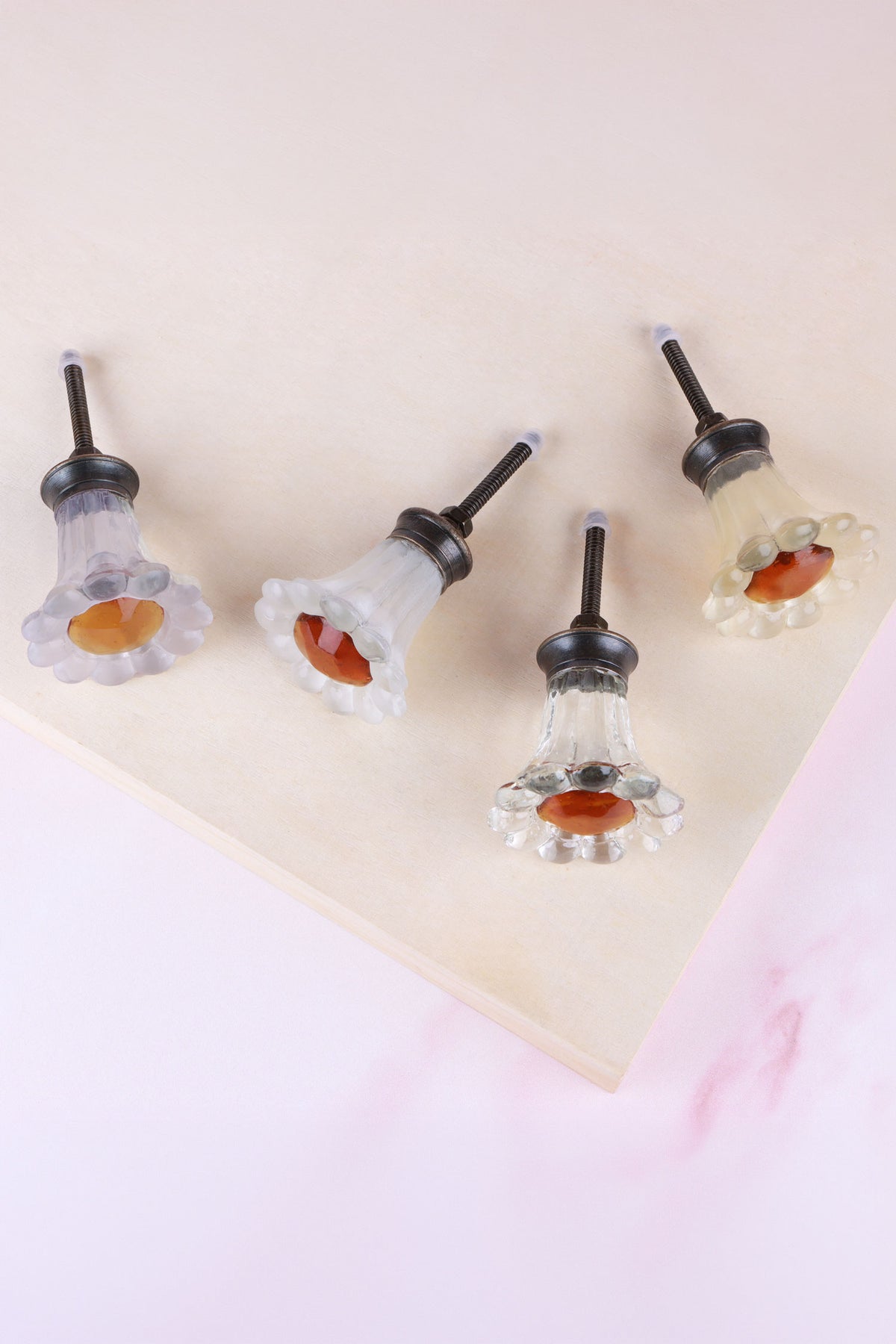 Four daisy glass knobs lying on their sides, showing the ribbed glass stems, antique brass finish bases and fixing bolts