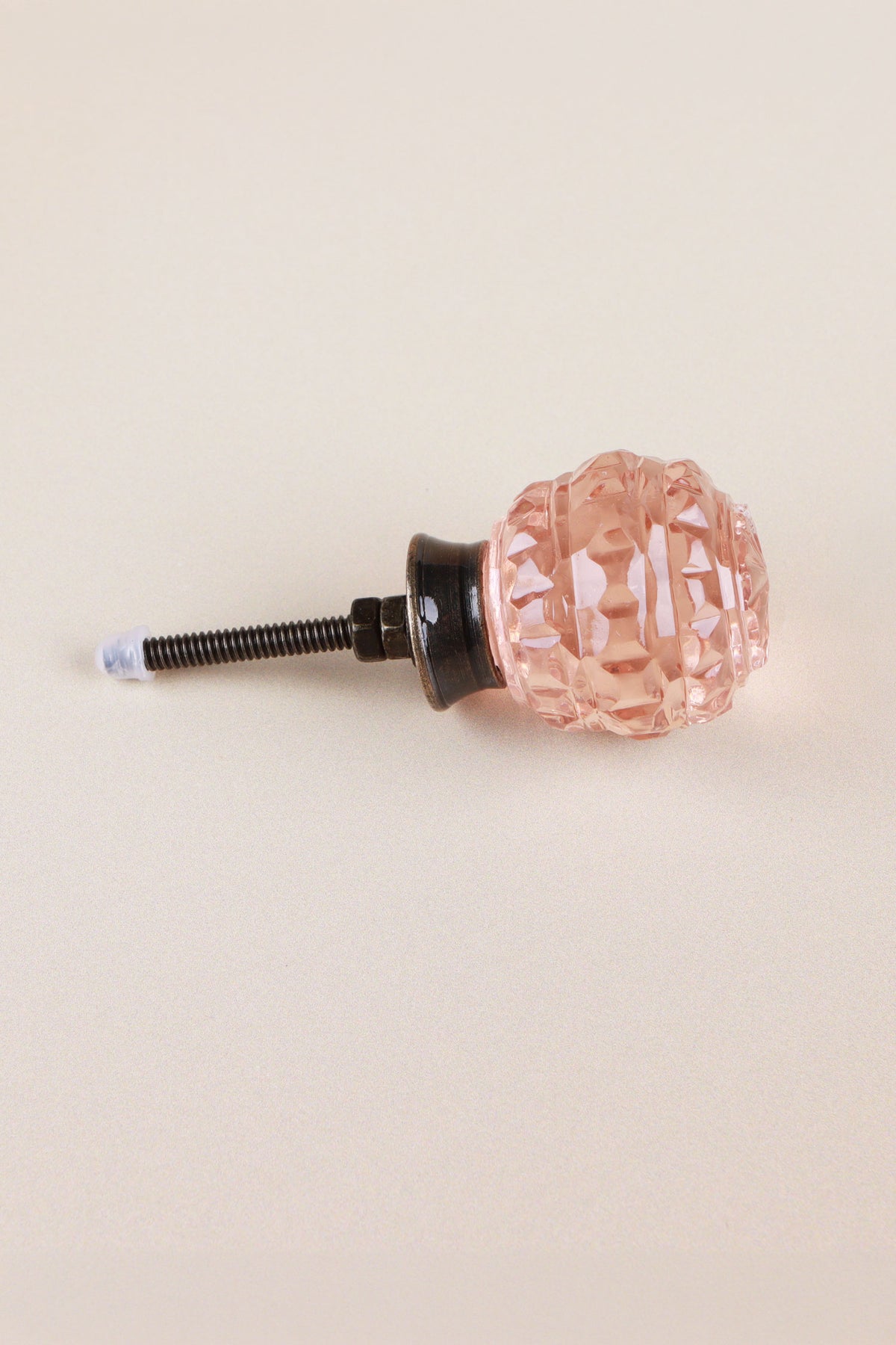 Side view of the blush pink faceted glass knob showing the antique brass finish base, the threaded fixing bolt and two nuts