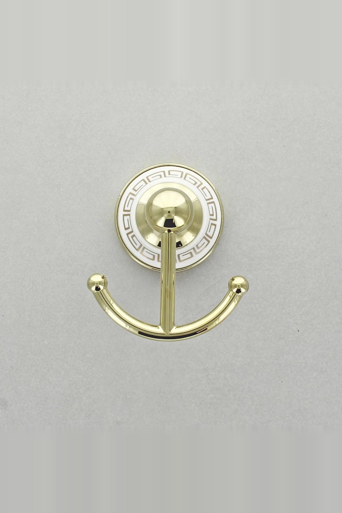 Gold double robe hook with two arms on a round white wall plate with a gold Greek key border