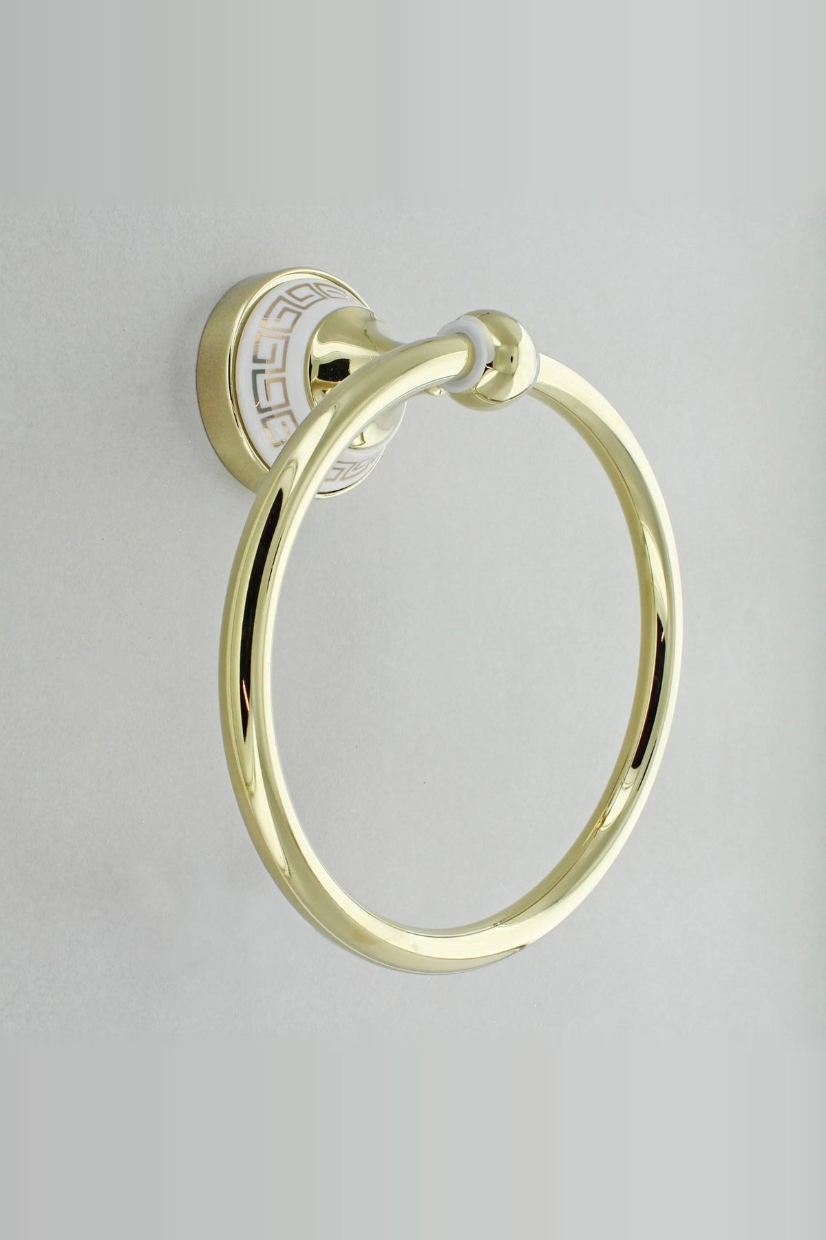 Gold towel ring on a round white wall plate with a gold Greek key border, on a grey tiled wall
