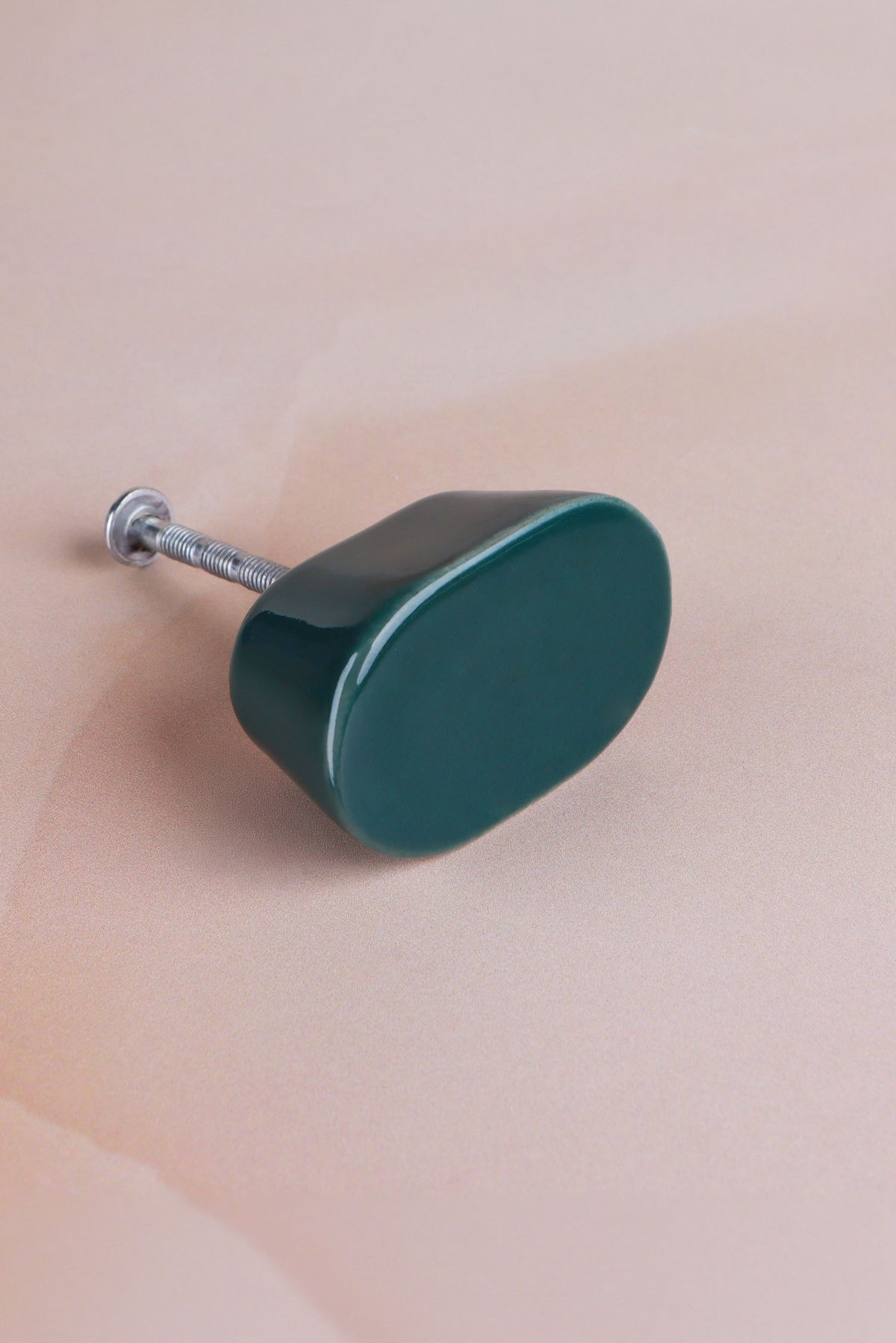 Dark teal oval ceramic cabinet knob, a deep glossy teal green, with its fixing bolt