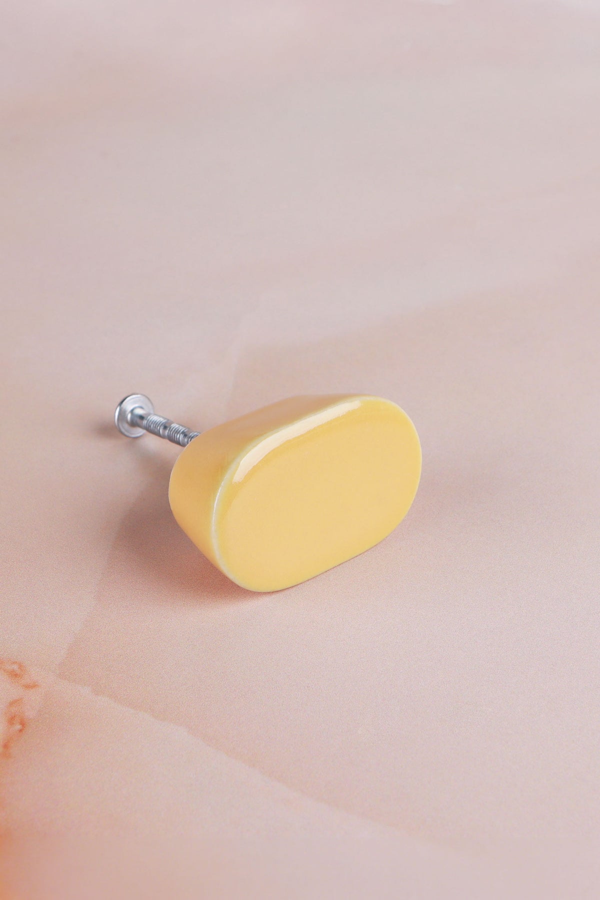 Yellow oval ceramic cabinet knob, a warm butter yellow, with its fixing bolt
