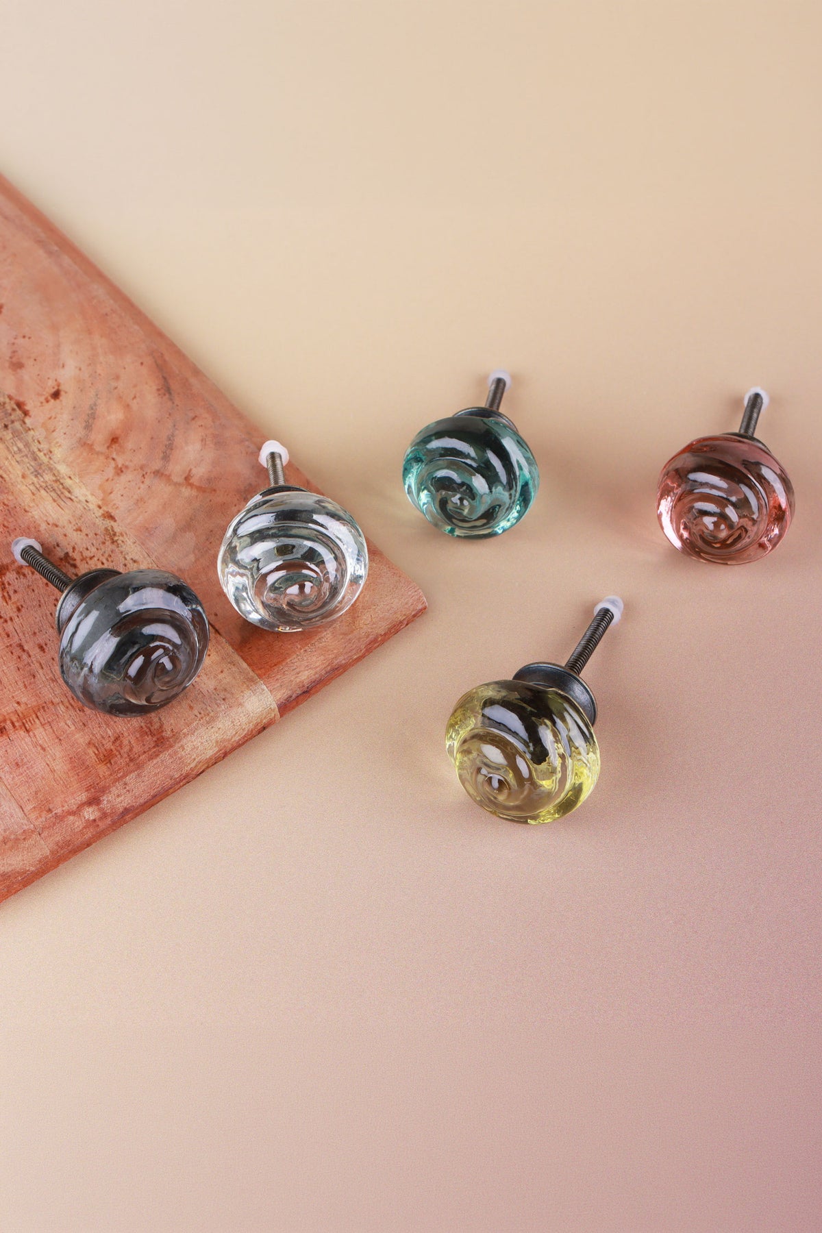 Small rose glass cabinet knobs in smokey grey, clear, teal, blush pink and ivory, two of them resting on a wooden board