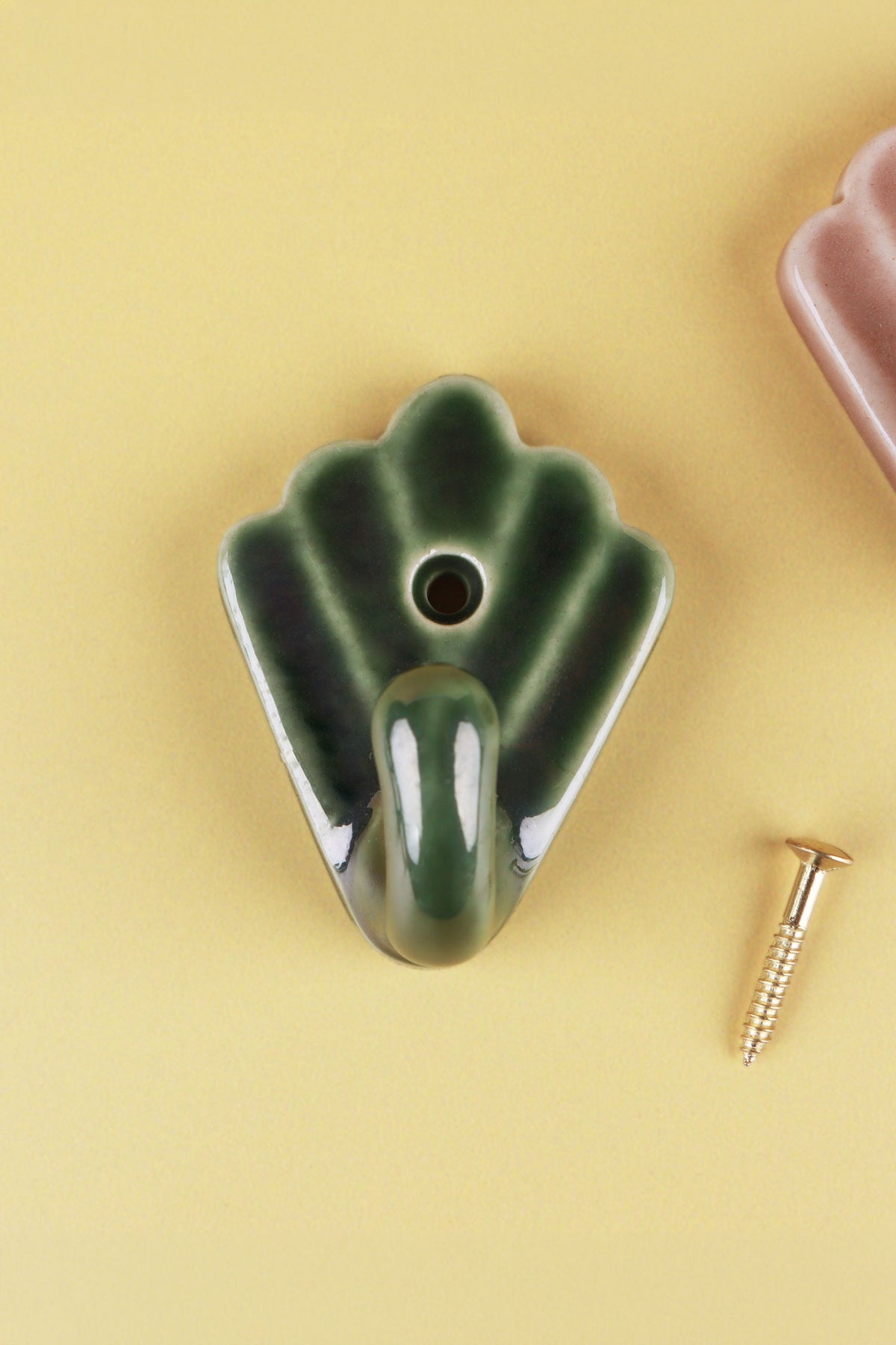 Olive green scallop shell ceramic wall hook, the glaze darker in the grooves, with its brass screw