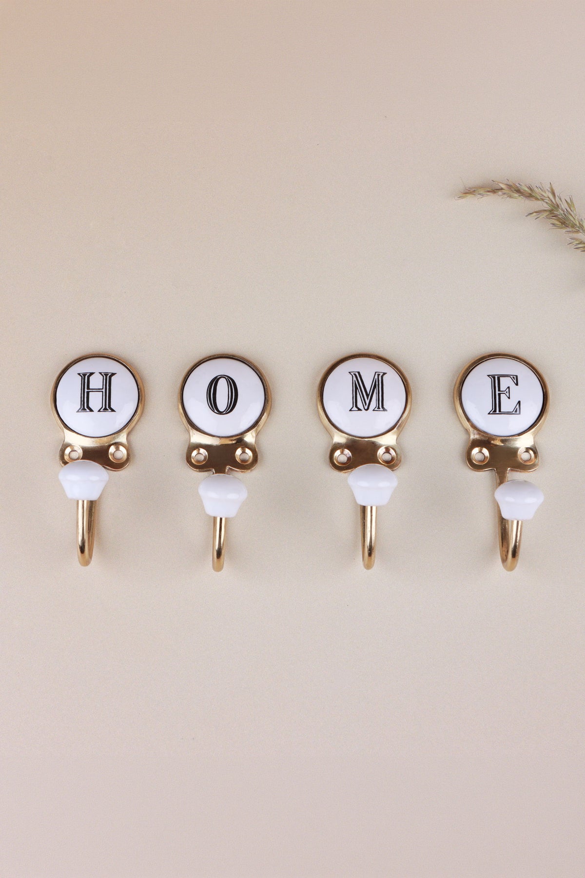 Four ceramic letter hooks in a row spelling HOME, white discs with black serif capitals in gold-tone frames and white ceramic knobs
