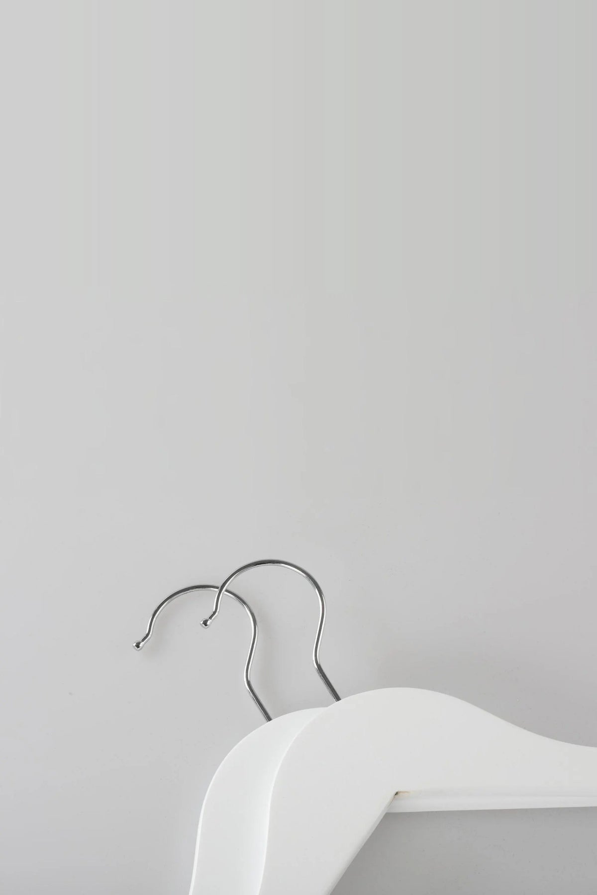 Close-up of two white wooden coat hangers showing the metal hooks