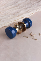 Navy blue ceramic mortice door knobs joined by the spindle through their polished brass roses, as they sit on a door