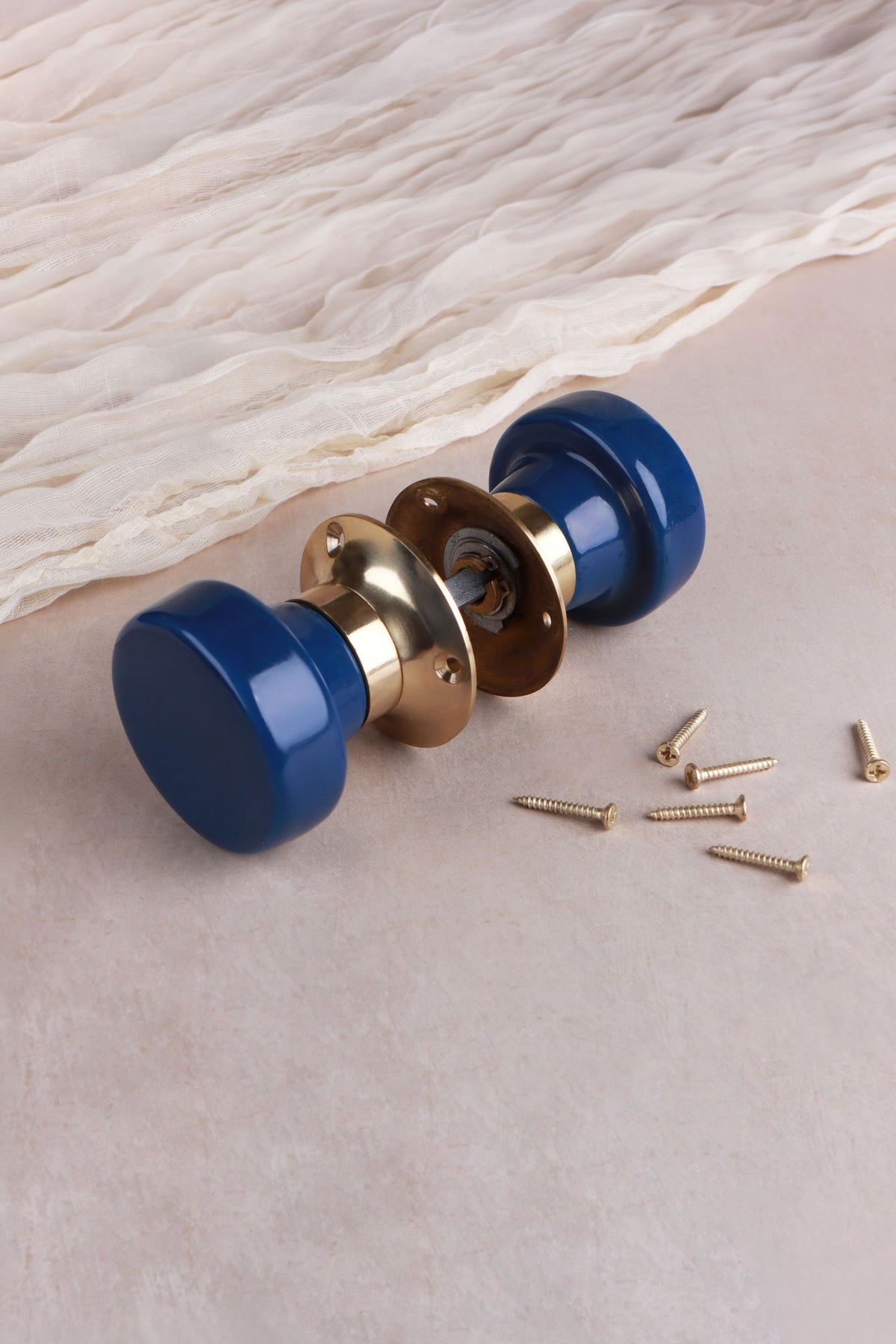 Navy blue ceramic mortice door knobs joined by the spindle through their polished brass roses, as they sit on a door