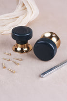 Charcoal ceramic door knob standing on its polished brass rose beside the second knob, with the spindle and fixing screws