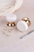 Cream ceramic door knob standing on its polished brass rose beside the second knob, with the spindle and fixing screws