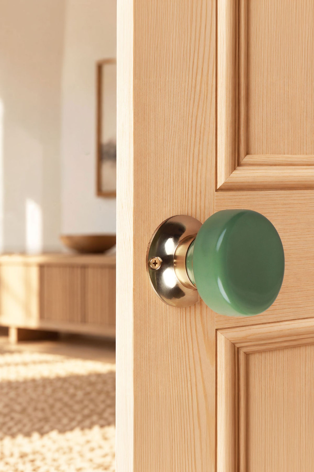 Sage green ceramic door knob on a polished brass rose, fitted to a wooden interior door