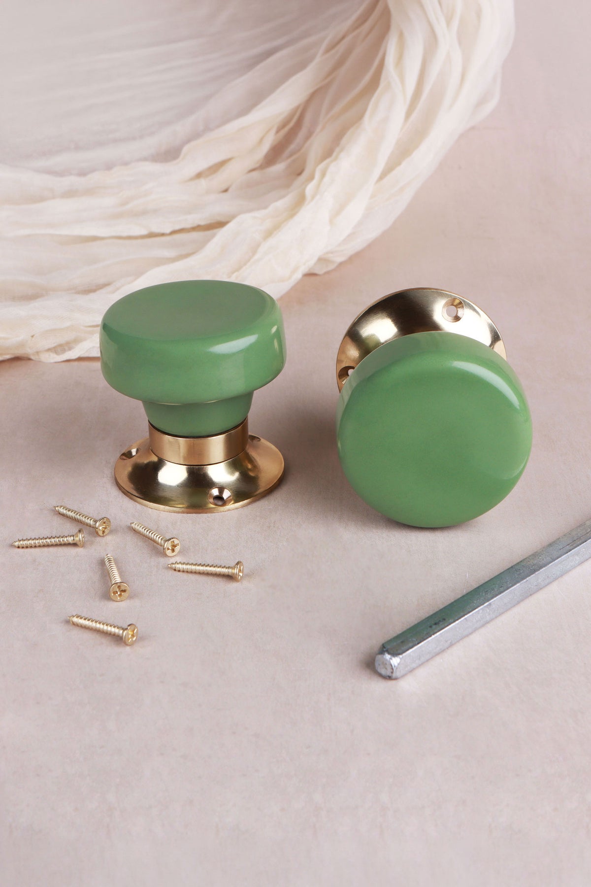 Pair of sage green ceramic mortice door knobs with flat faces on polished brass roses, with the 8 mm spindle and fixing screws