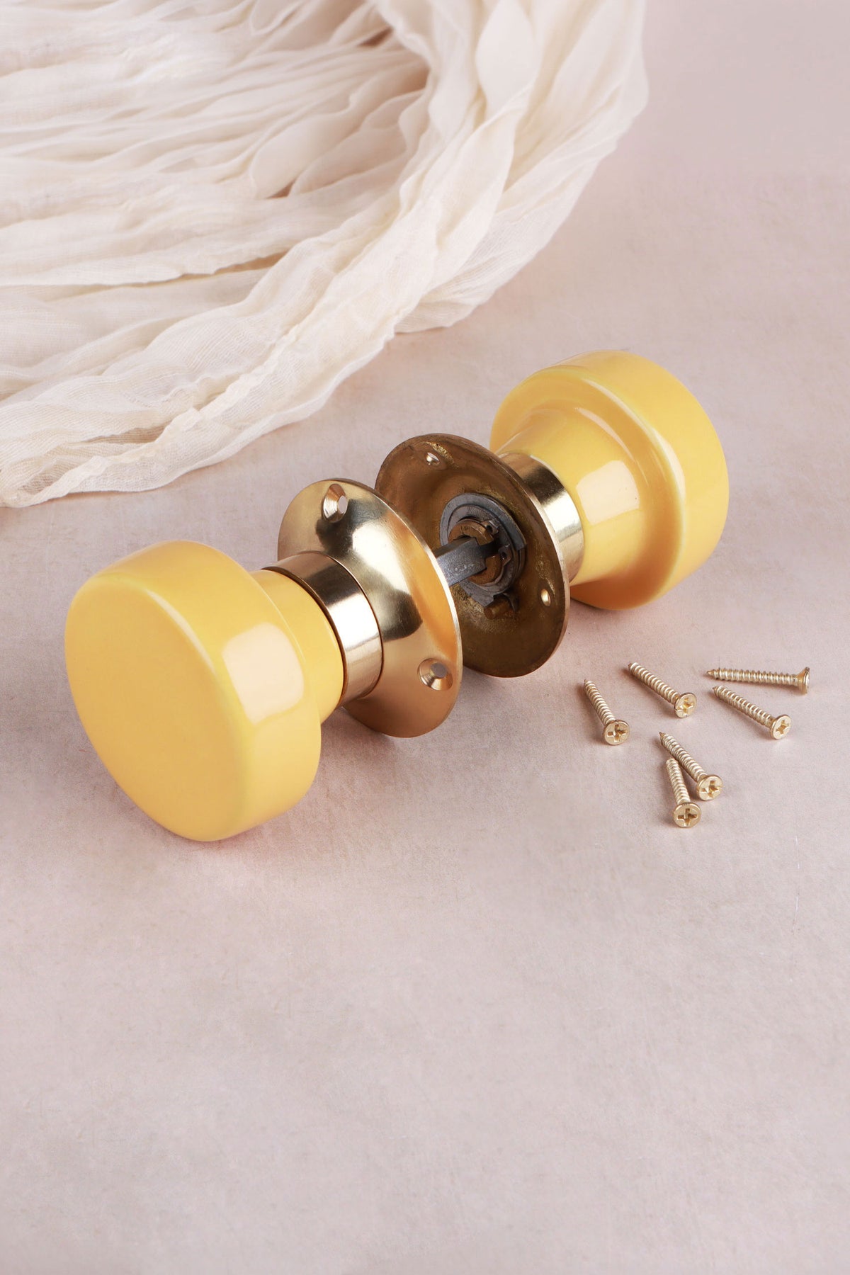 Yellow ceramic mortice door knobs joined by the spindle through their polished brass roses, as they sit on a door