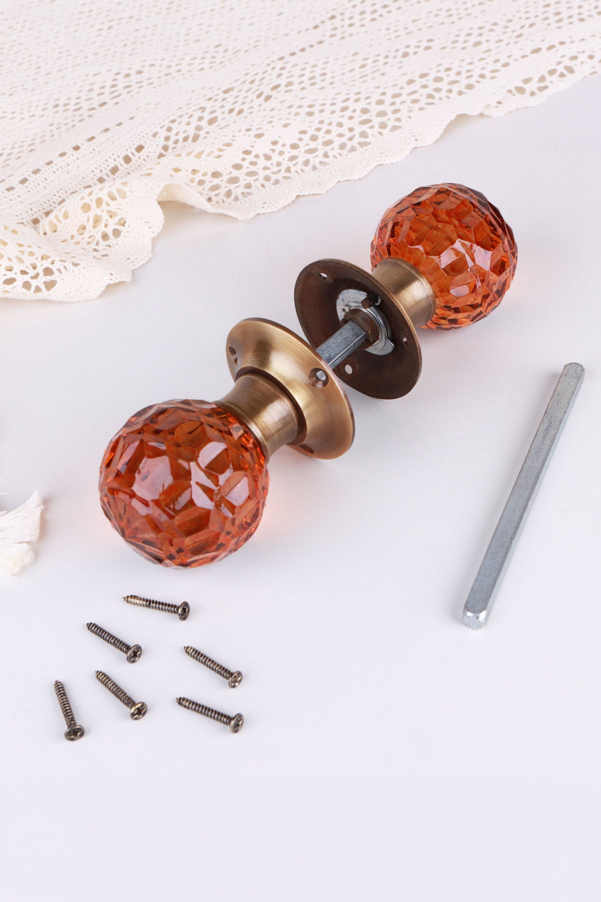 Amber glass mortice door knobs joined by the spindle through their antique brass roses, as they sit on a door