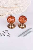 Pair of amber faceted glass mortice door knobs on antique brass roses, with the square spindles and fixing screws
