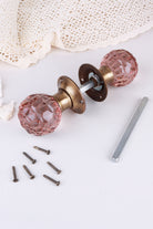 Blush Pink glass mortice door knobs joined by the spindle through their antique brass roses, as they sit on a door