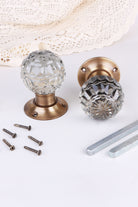 Clear Crystal faceted glass door knob standing on its antique brass rose beside the second knob lying on its side, with the spindles and screws