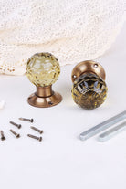 Ivory faceted glass door knob standing on its antique brass rose beside the second knob lying on its side, with the spindles and screws