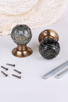 Smokey Grey faceted glass door knob standing on its antique brass rose beside the second knob lying on its side, with the spindles and screws