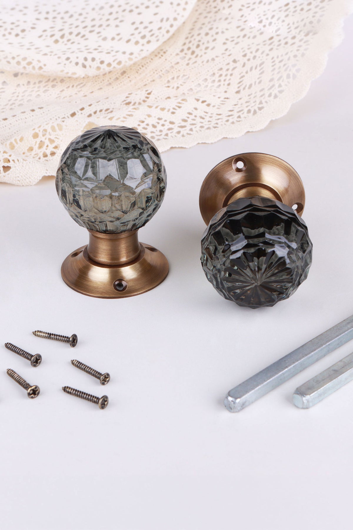 Smokey Grey faceted glass door knob standing on its antique brass rose beside the second knob lying on its side, with the spindles and screws