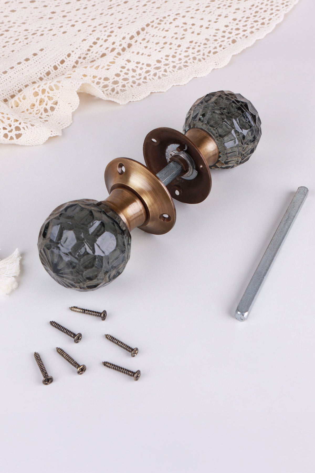 Smokey Grey glass mortice door knobs joined by the spindle through their antique brass roses, as they sit on a door