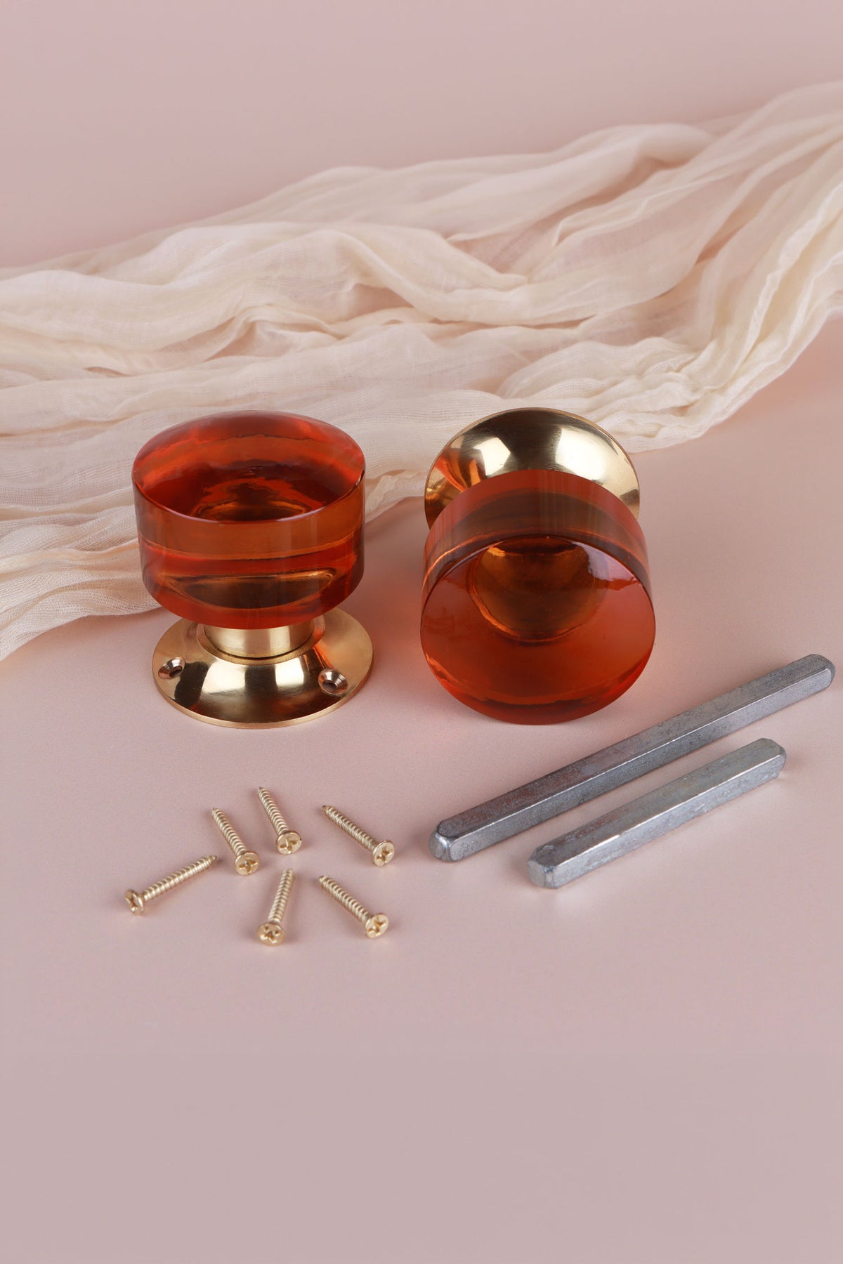 Pair of amber glass cylinder mortice door knobs on polished brass roses, one standing and one on its side, with the square spindles and fixing screws