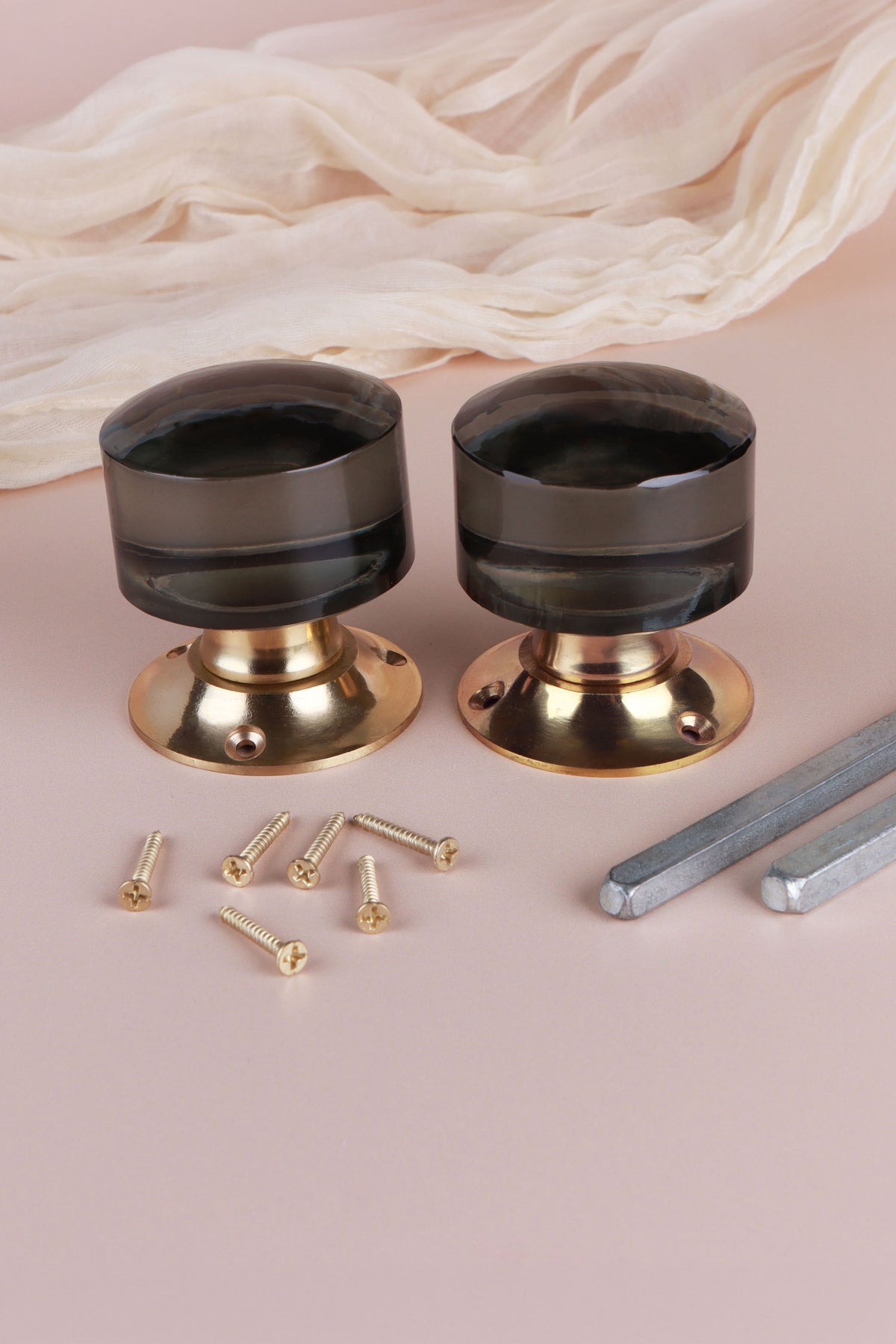 Two smokey grey glass cylinder door knobs standing on their polished brass roses, with the square spindles and fixing screws