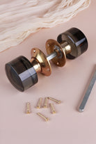 Smokey grey glass cylinder mortice door knobs joined by the spindle through their polished brass roses, as they sit on a door
