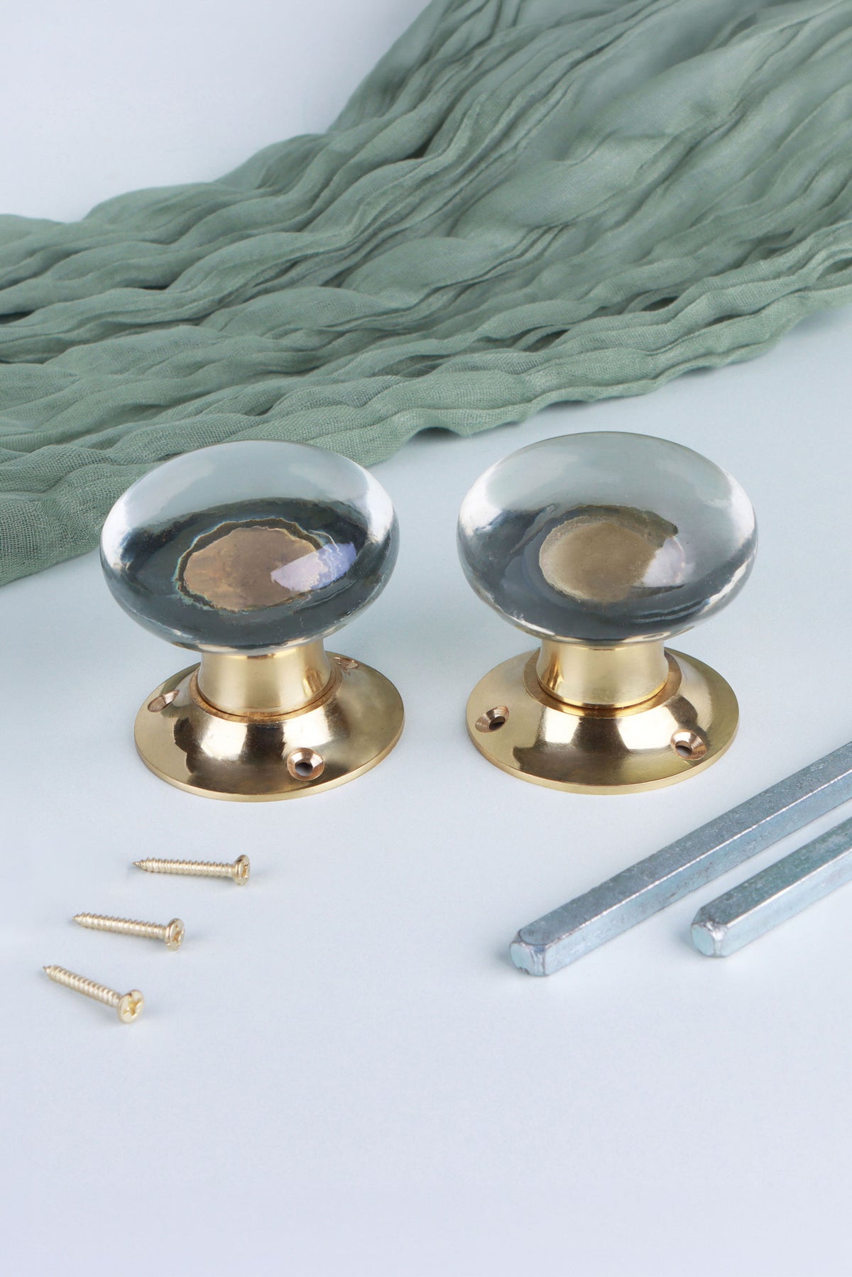 Two clear glass dome door knobs standing on their polished brass roses, with the square spindles and fixing screws