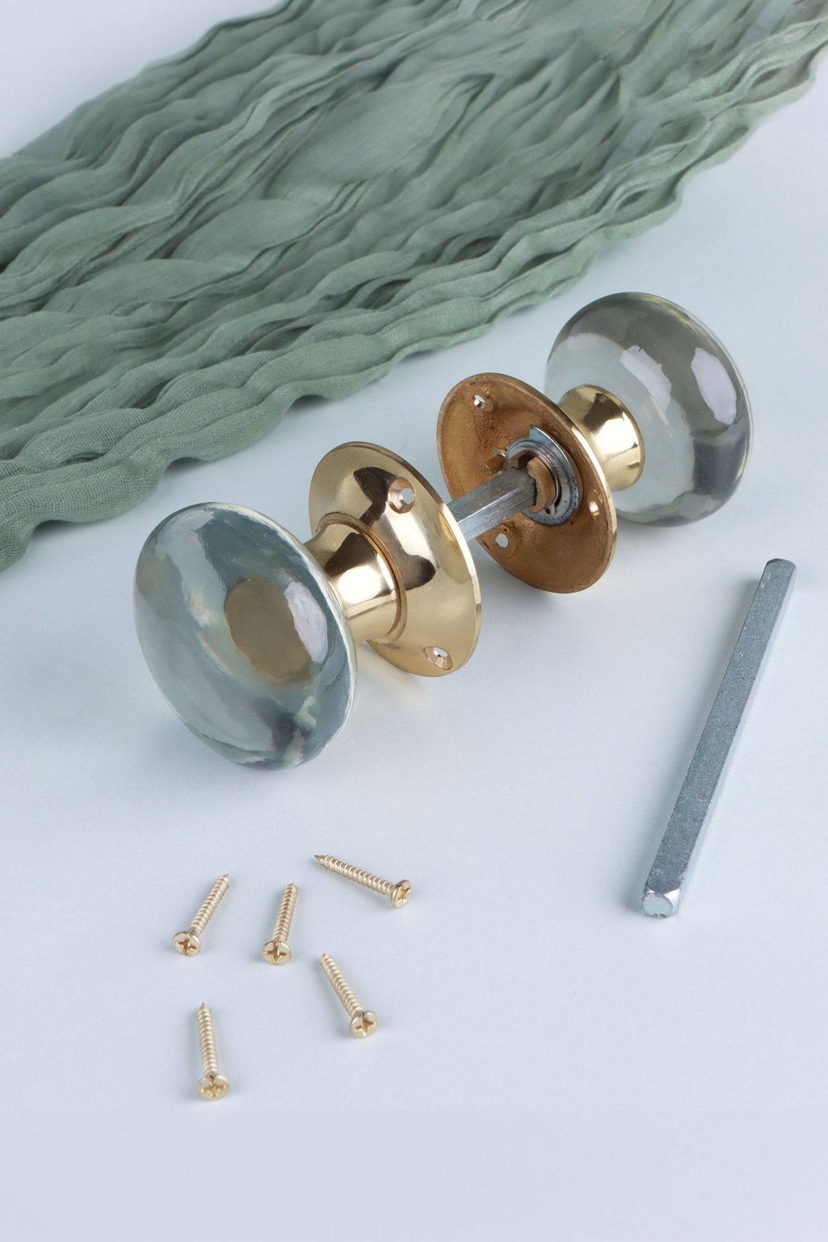 Clear glass dome mortice door knobs joined by the spindle through their polished brass roses, as they sit on a door