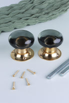 Two smokey grey glass dome door knobs standing on their polished brass roses, with the square spindles and fixing screws