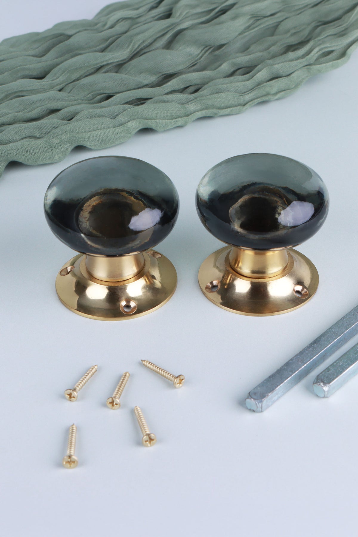 Two smokey grey glass dome door knobs standing on their polished brass roses, with the square spindles and fixing screws