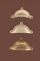 Classic brass cup pull handles grouped, showing the deep bowl and rounded lugs