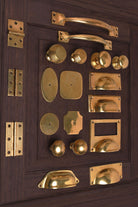 The complete aged brass cabinet hardware set laid out on a panelled door — knobs, cup pulls, rosettes, hinges and pull handles