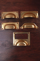 Five aged brass cup pull shapes — bevelled plate, square plate, rounded plate, classic and card frame