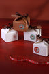 Festive gift boxes with brown ribbons and holiday stickers, styled on a red background from G Decor.