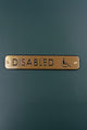 Gold metal disabled access sign with wheelchair symbol on dark green wall, G Decor hardware