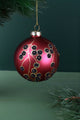 Luxury red Christmas bauble with gold and black floral design, hanging from pine branch