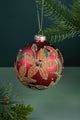 Red glass Christmas bauble with gold glitter floral design hanging on a pine tree branch