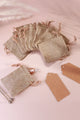 Rustic burlap gift bags with drawstrings and kraft tags on a soft pink background, G Decor
