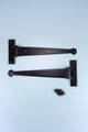 Pair of black metal T hinges with screws on light background, G Decor hardware.