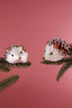 Two hedgehog Christmas ornaments on pine branches, pink background, G Decor home décor