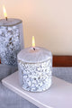 Decorative textured white pillar candle with leaf pattern lit on a grey table, G Decor home décor