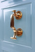 Polished gold door knocker on a paneled light blue door from G Decor luxury hardware.