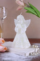 White angel candle with snowflake design, flowers, pearls, and glassware on wooden table, G Decor
