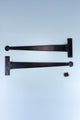 Pair of black metal T-hinges with screws, G Decor luxury hardware on light blue background.